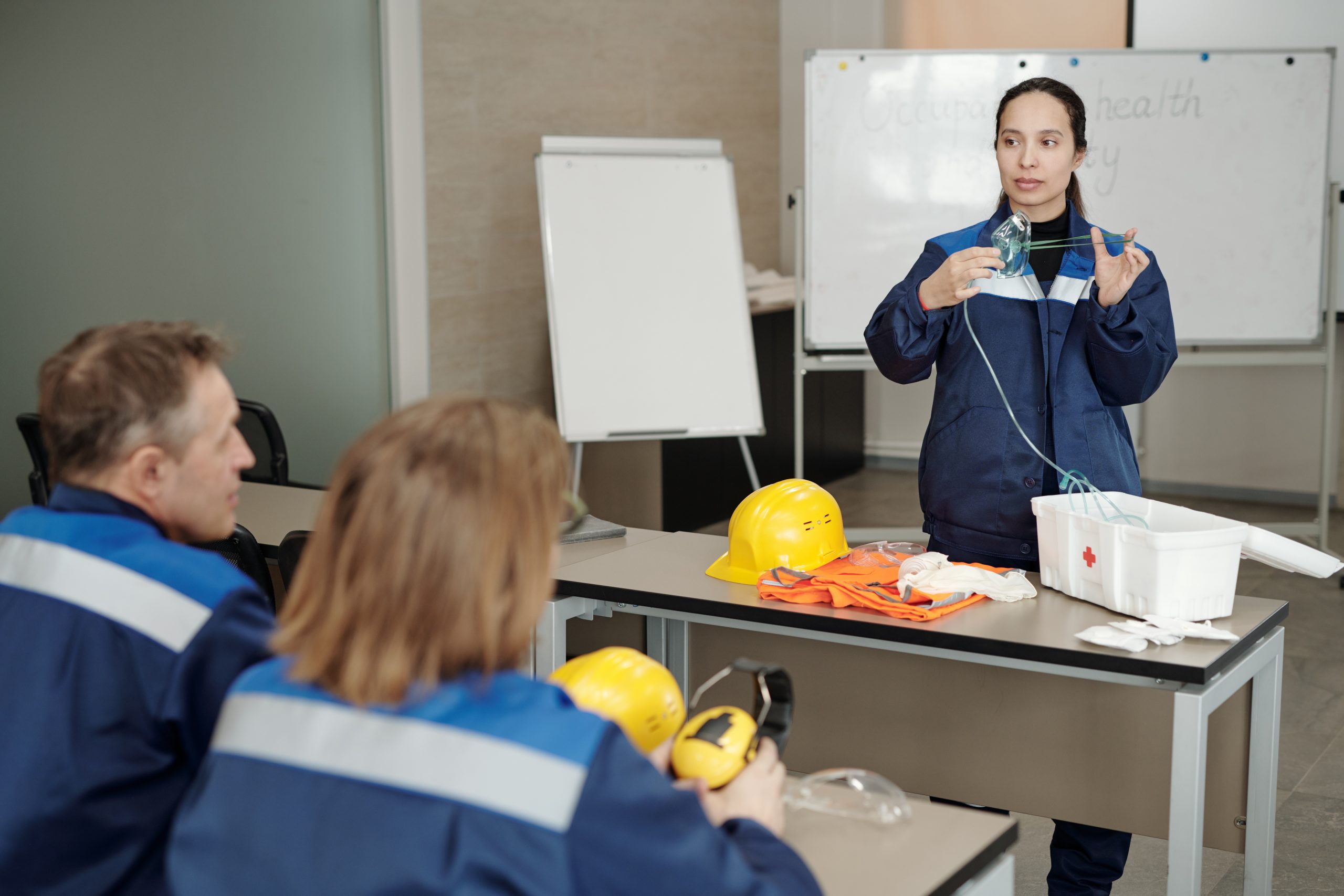 Young female worker demonstrating usage of respirator while standing by desk in front of colleagues during basics of life safety lesson